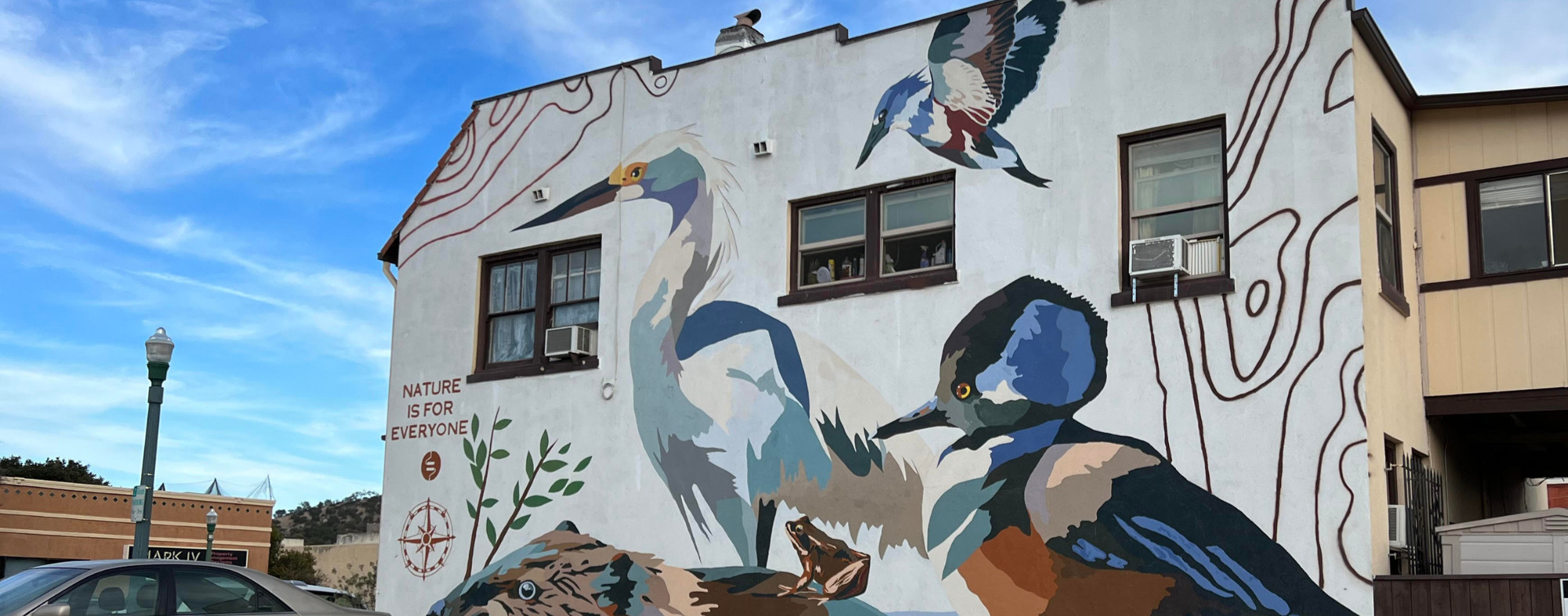 Mural featuring birds and native wildlife with the words "Nature Is for Everyone" on a building.