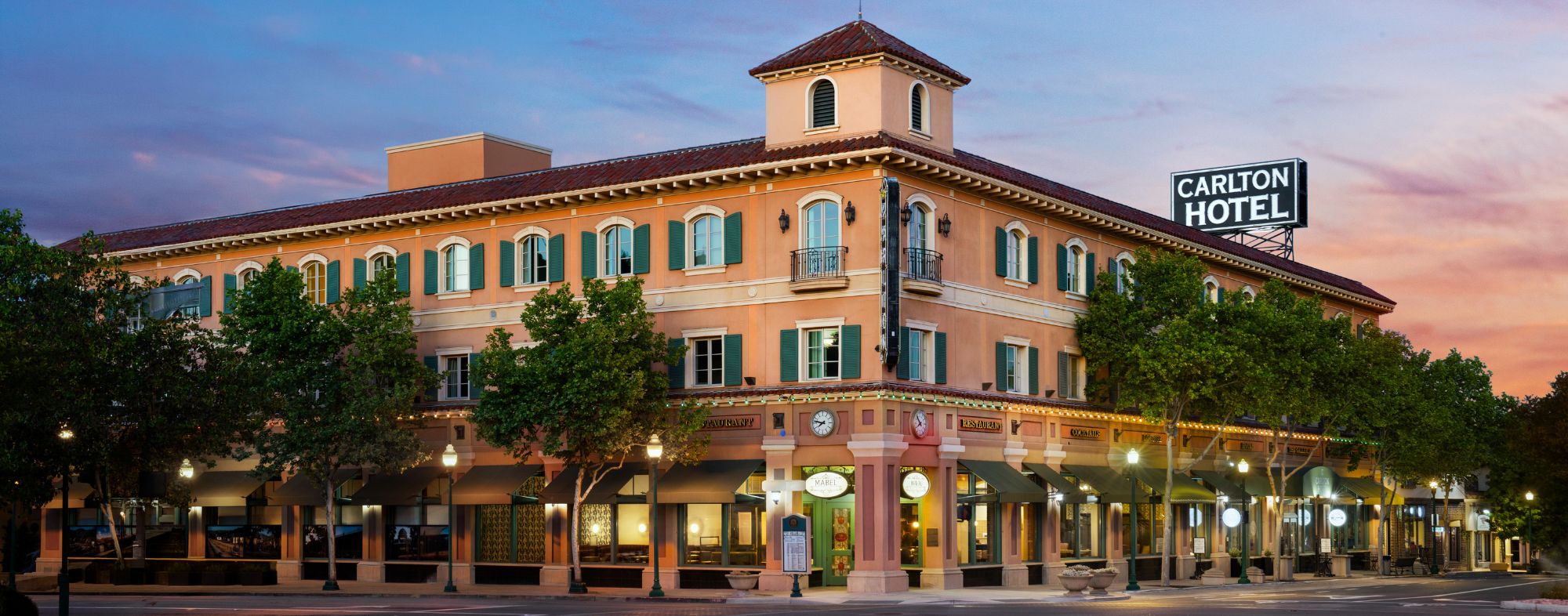 Exterior of the Carlton Hotel at the corner of El Camino Real with ground-floor restaurants.
