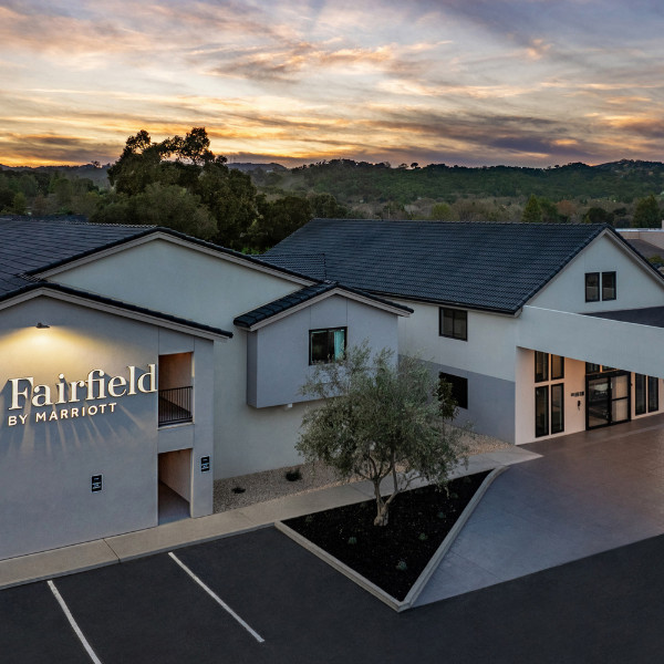 Photo of Fairfield hotel gray building with rolling green hills and sunset in background and trees out front in parking lot