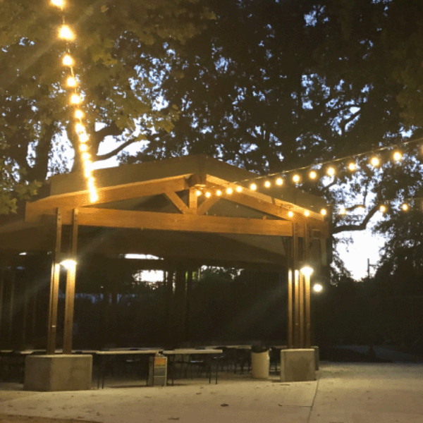 Open-air event pavilion with guests, vendor tables, and wood-beam architecture.