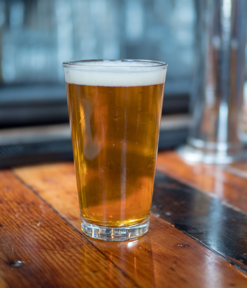 Full pint of golden beer sitting on a rustic wooden bar 